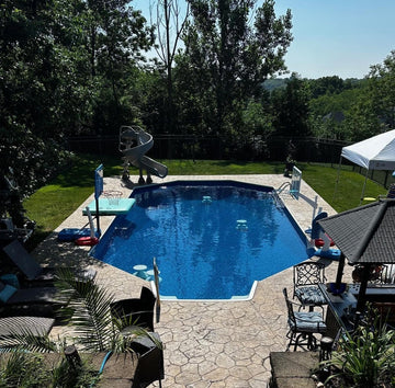 Stone steps leading to a backyard pool with a slide, surrounded by green lawn and shaded seating areas