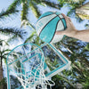 Close-up of hand dunking blue and white waterproof basketball into Dunn-Rite Deck Shoot hoop, with palm trees in background