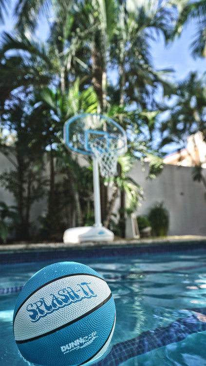 Floating Splash-It ball in foreground with pool basketball hoop and palm trees in background