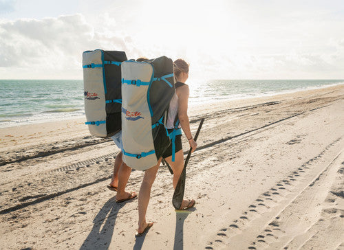 Two paddle boarders walking along the beach with Dunn Rite SUP backpacks and paddles